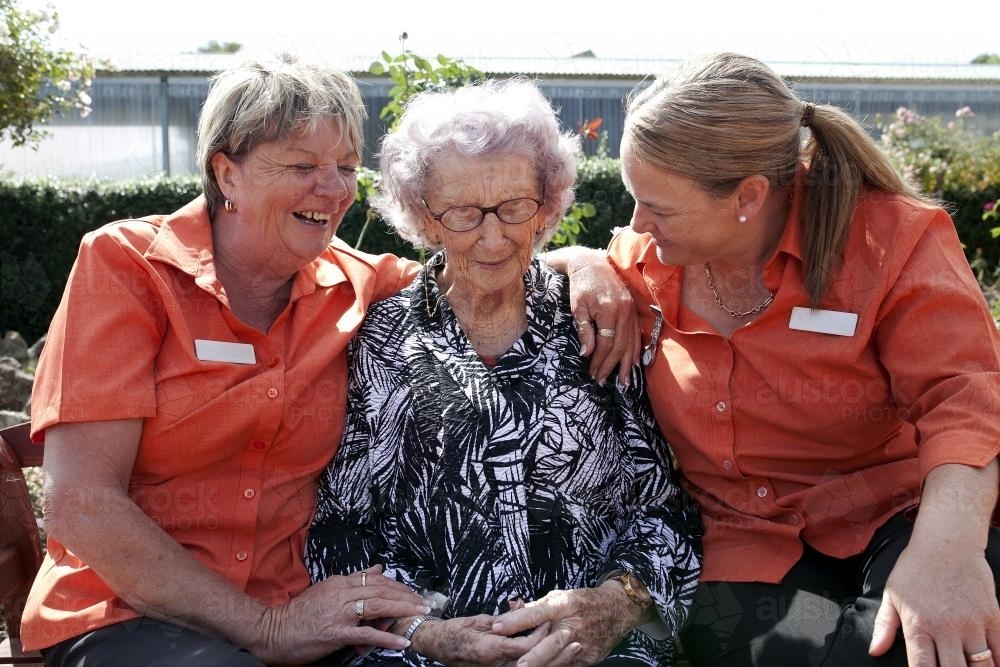 Elderly lady sitting outside between two carers at aged care facility - Australian Stock Image
