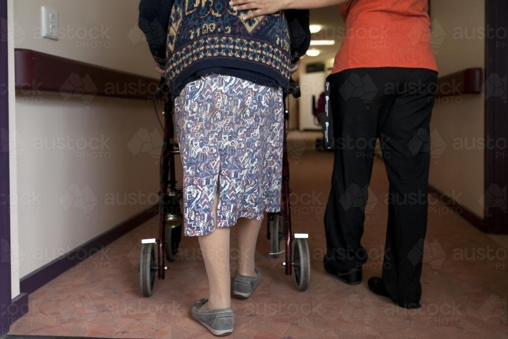 Elderly lady walking down corridor with help from nurse - Australian Stock Image
