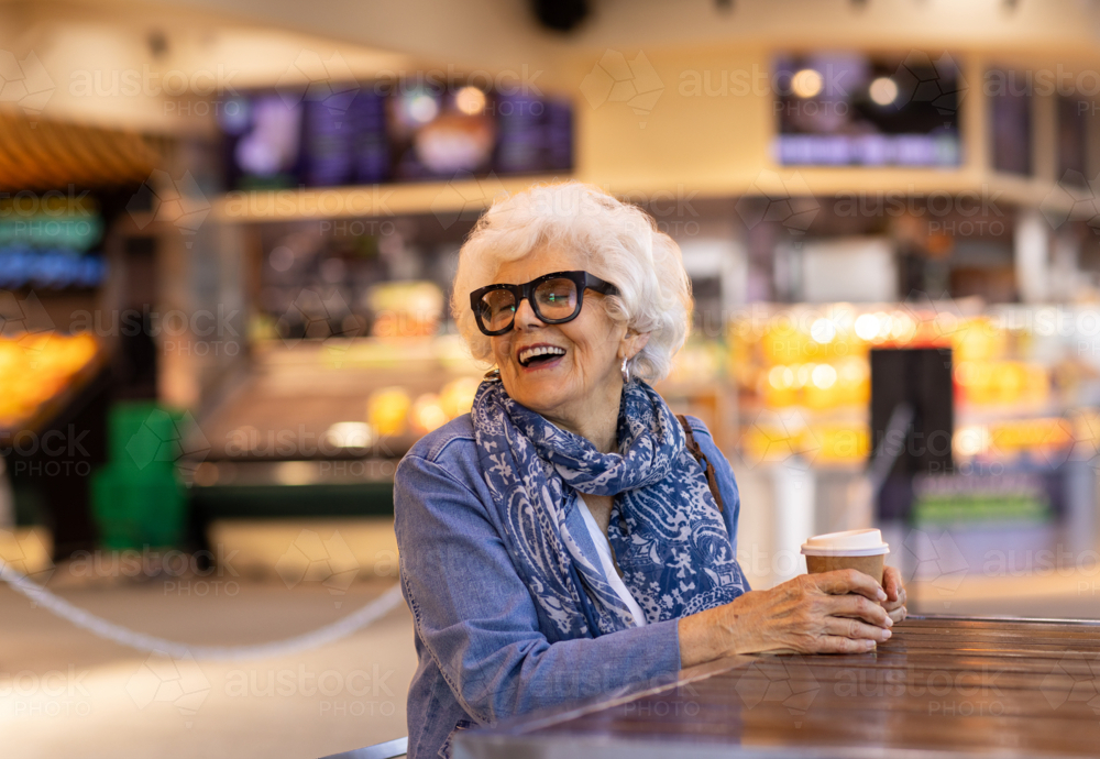 elderly lady with coffee in mall cafe - Australian Stock Image