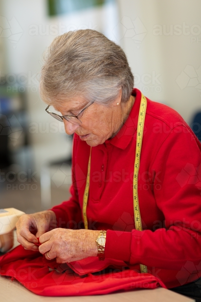 elderly lady working on sewing project in red fabric - Australian Stock Image