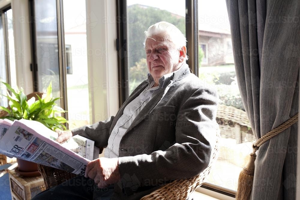 Elderly male retirement village resident reads paper by the window - Australian Stock Image