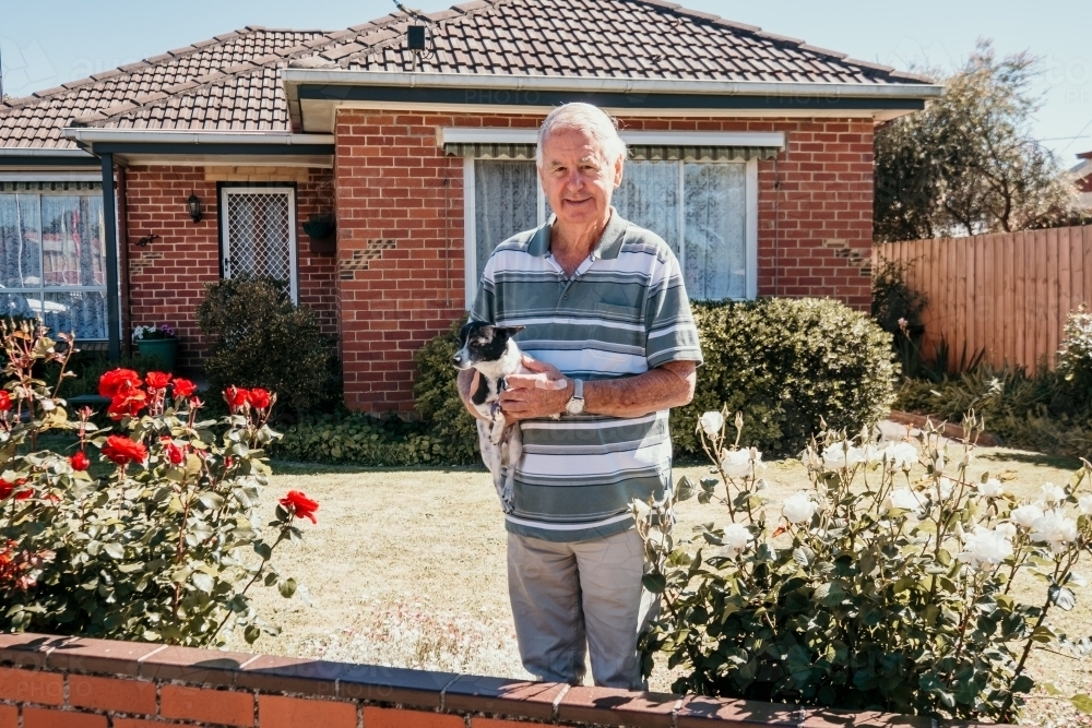 Elderly man and his little dog stand at the fence in front of his house. - Australian Stock Image