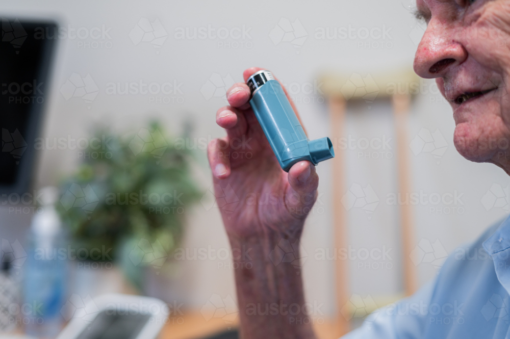 Elderly man holding an inhaler while seated in clinic - Australian Stock Image