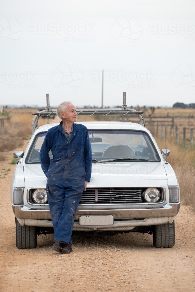 Elderly man leans on his car bonnet on a dusty road. - Australian Stock Image