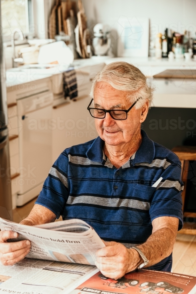 Elderly man reading newspaper in the kitchen. - Australian Stock Image