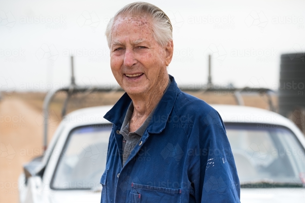 Elderly man smiling on a dusty dirt road. - Australian Stock Image