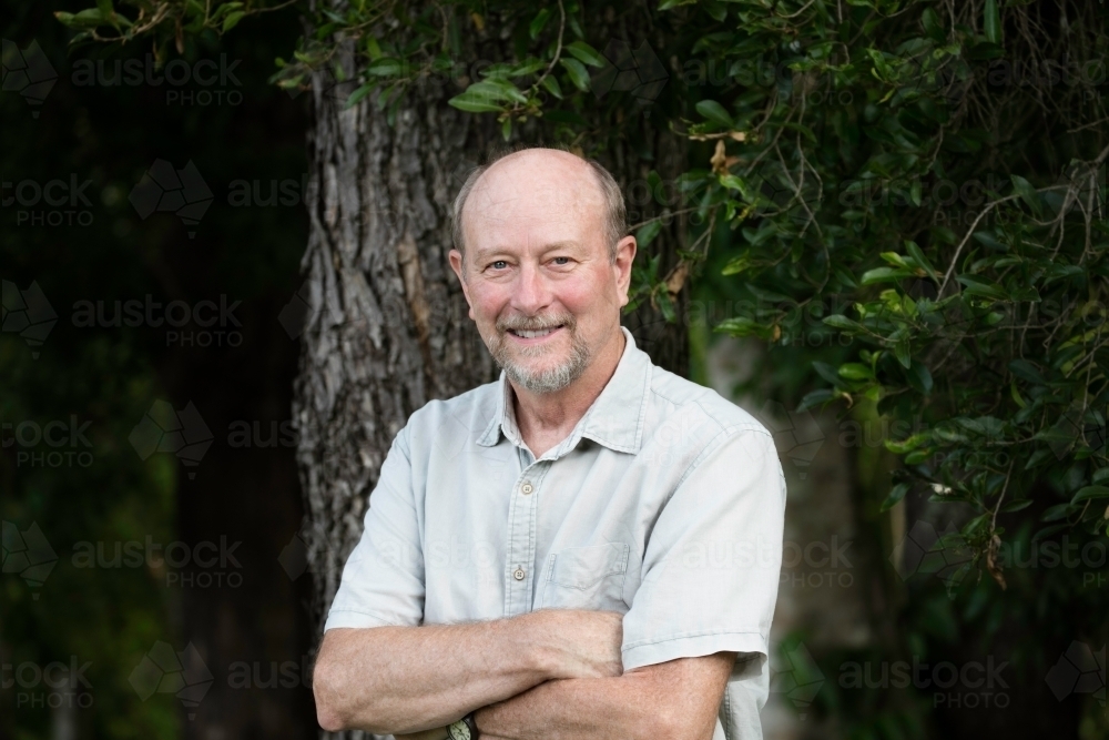 Elderly man smiling with arms folded looking at camera - Australian Stock Image