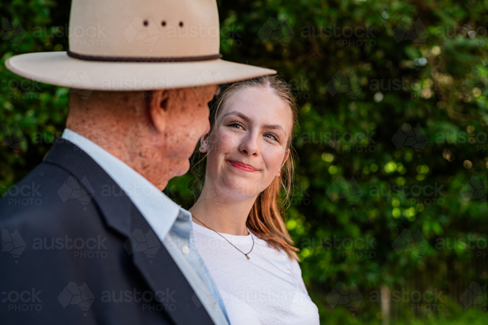 Elderly man wearing wide brimmed hat walking with his granddaughter outdoors looking at each other - Australian Stock Image