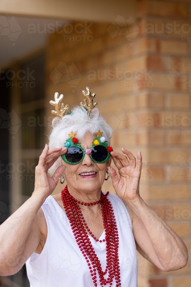 Elderly white-haired lady wearing decorative Christmas glasses and headband with beads around neck - Australian Stock Image