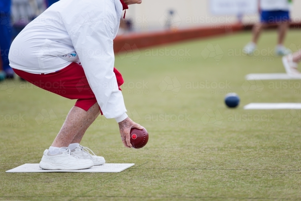 Elderly woman crouching before delivering a lawn bowl - Australian Stock Image