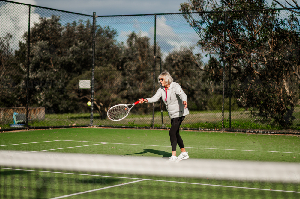 Elderly woman enjoying a tennis match on a green court outdoors - Australian Stock Image