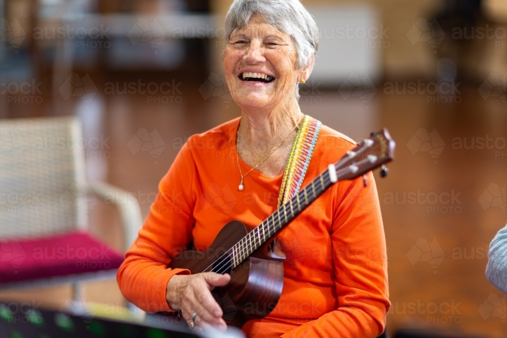 elderly woman holding ukulele and laughing - Australian Stock Image