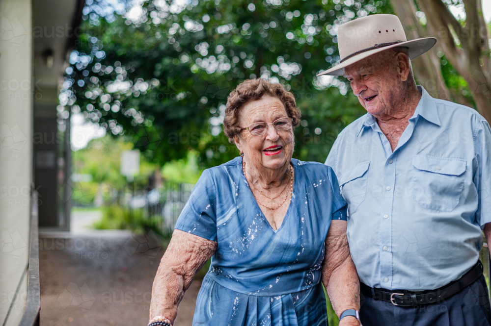 Elderly woman in blue patterned dress walking with an elderly man outdoors - Australian Stock Image