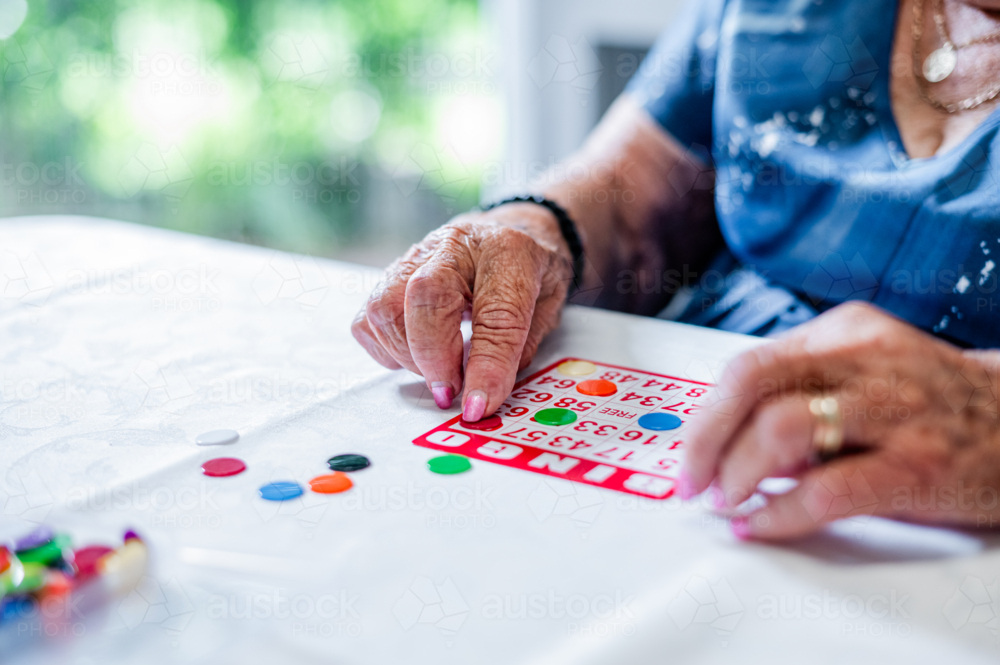 Elderly woman playing bingo cards on the table - Australian Stock Image