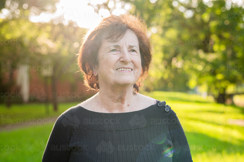 Elderly woman standing outdoors with soft sunlight glow - Australian Stock Image