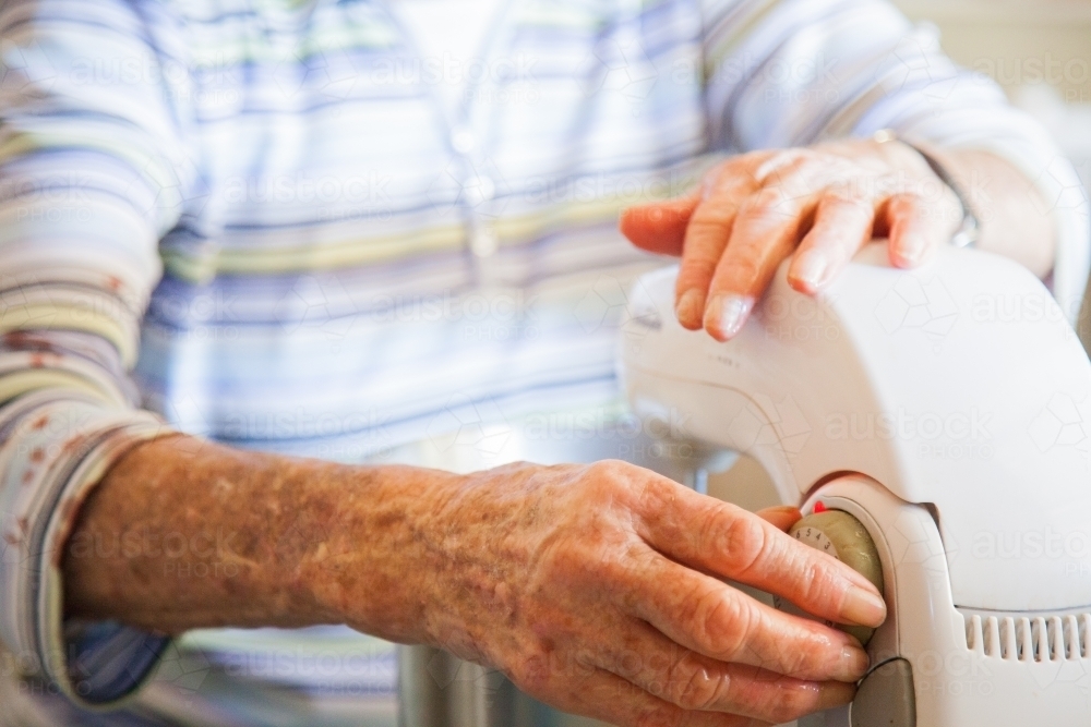 Elderly woman turning on mixer to make a sponge cake - Australian Stock Image
