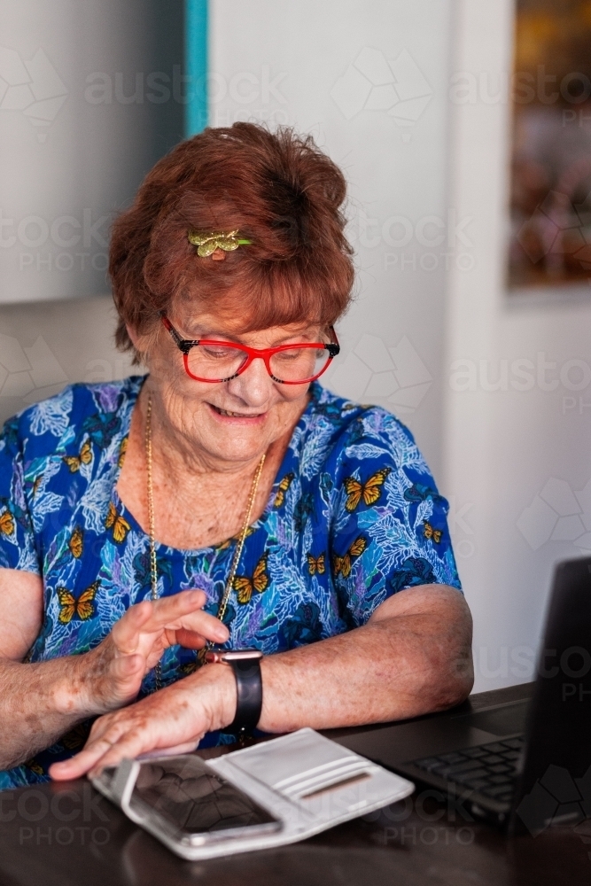 Elderly woman using technology wearing smartwatch connected to her mobile - Australian Stock Image