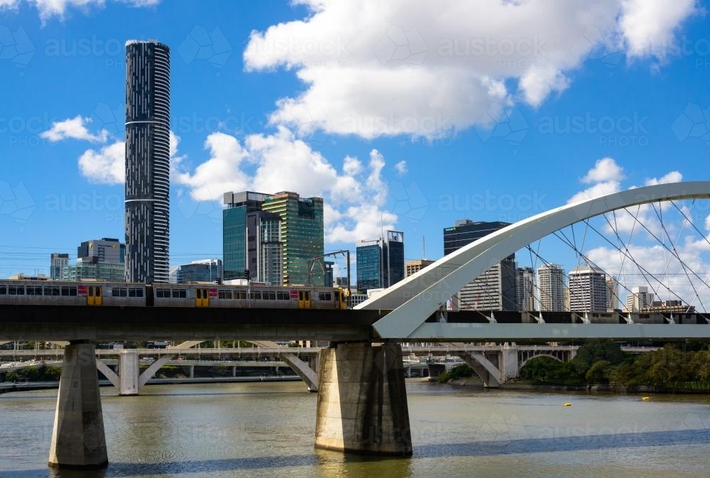 Electric train crossing railway bridge over Brisbane River with city skyline in background - Australian Stock Image