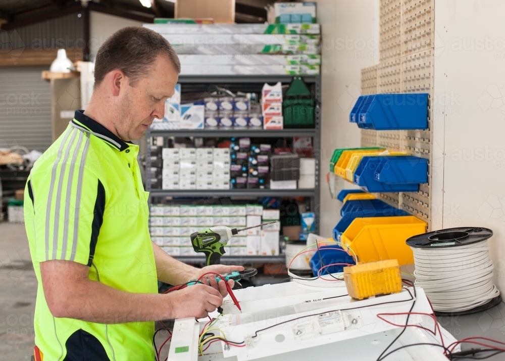 Electrician testing current with multimeter in his workshed - Australian Stock Image