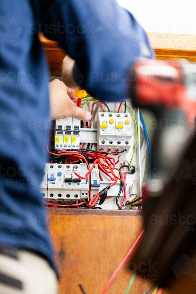 Electrician tradesman rewiring switch board for solar power - Australian Stock Image