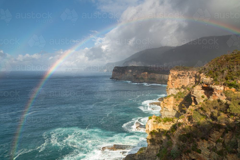Elevated view of a double rainbow and dark storm clouds over rugged coastal cliffs - Australian Stock Image