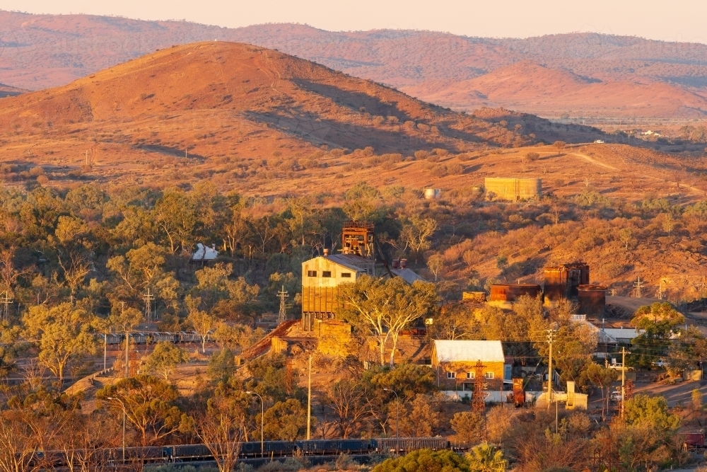 Elevated view of of mine buildings in front of barren hills in golden evening light - Australian Stock Image