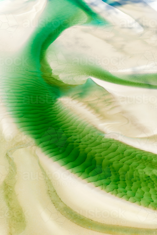 Emerald tidal patterns winding across pale sand flats. - Australian Stock Image