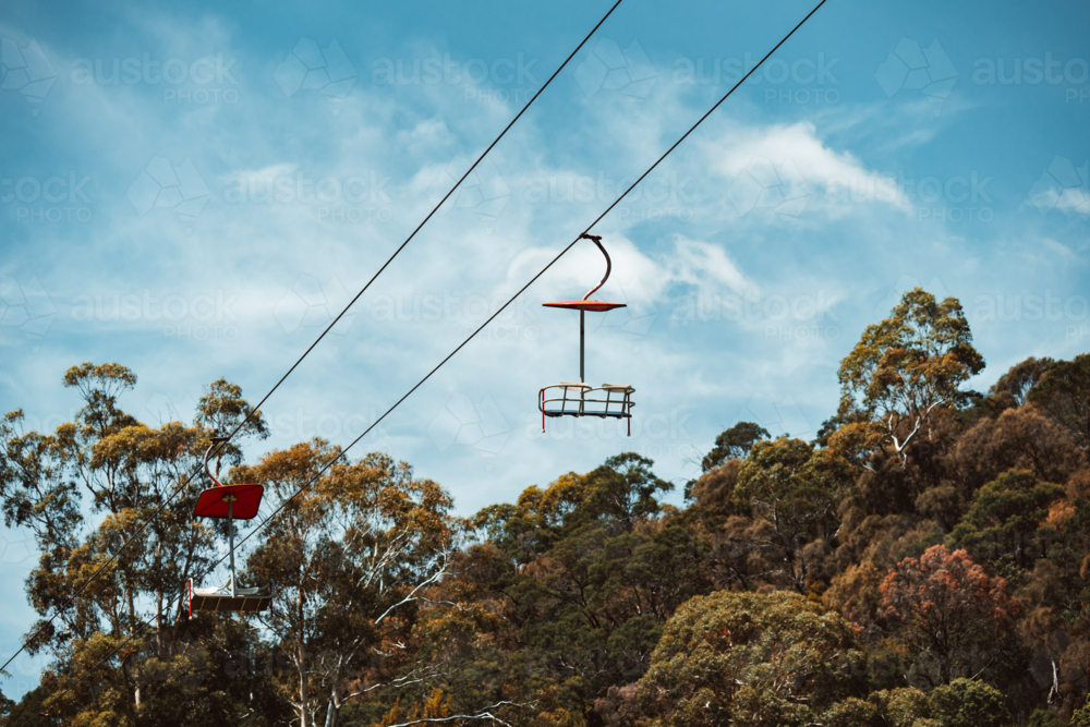 Empty chairlift gliding on steel cable above treetops. - Australian Stock Image
