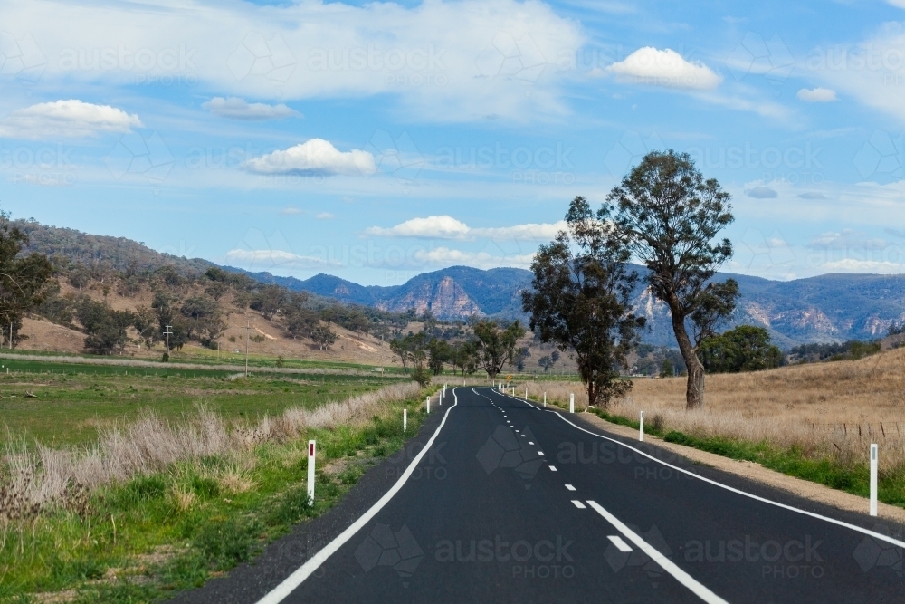 Empty road through farmland landscape to hills - Australian Stock Image