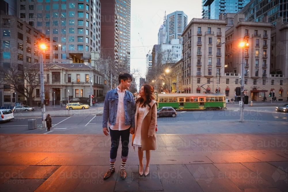 Engaged couple embracing in the city with Melbourne cityscape in background at night - Australian Stock Image