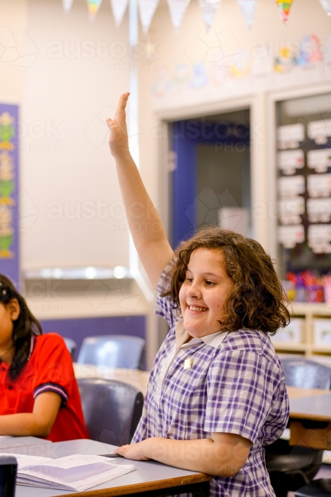 Enthusiastic girl student with her hand up in the classroom - Australian Stock Image