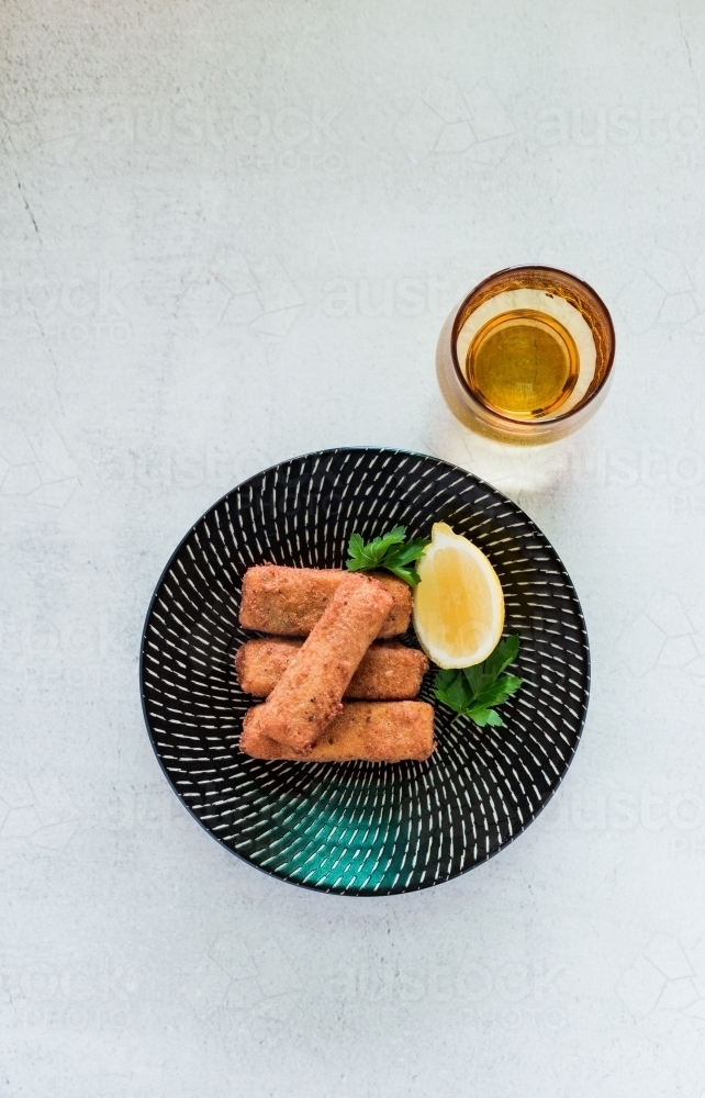 Entree of polenta wedges stacked on a black plate with a lemon and glass of beer - Australian Stock Image