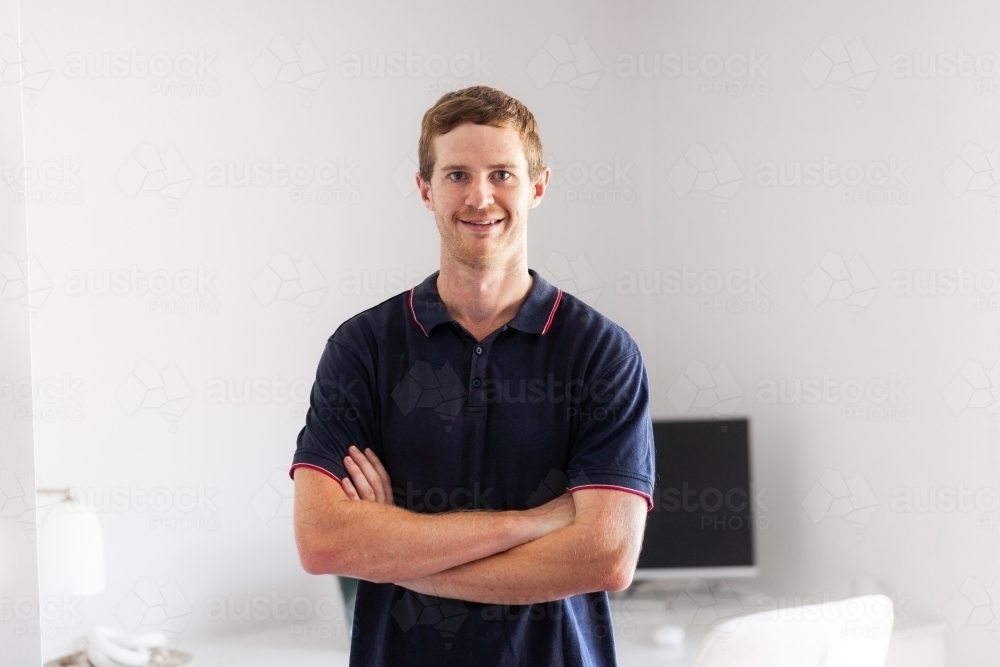 Environmental portrait of young man in his twenties standing with home office behind - Australian Stock Image