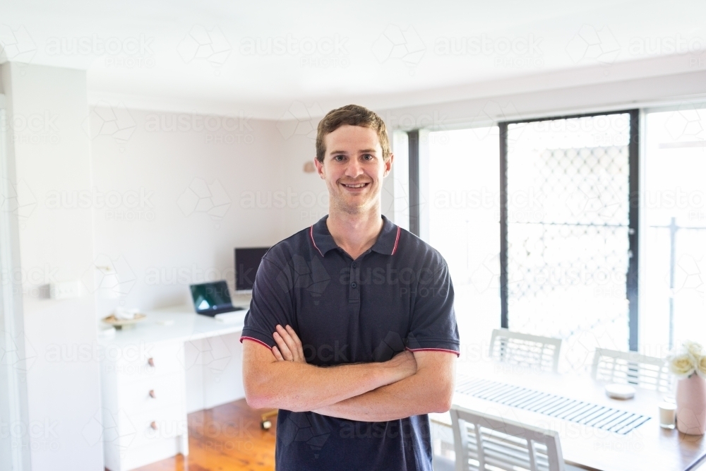 Environmental portrait of young man in his twenties standing with home office behind - Australian Stock Image