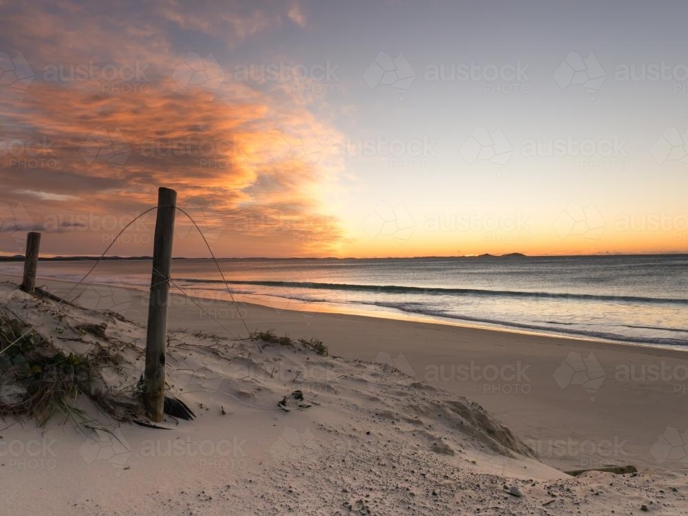 Eroded beach before sunrise with orange clouds - Australian Stock Image