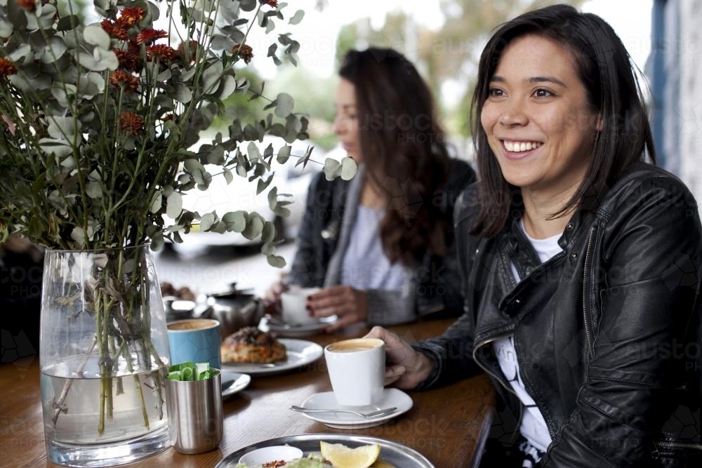 Eurasian woman at cafe smiling and looking away - Australian Stock Image