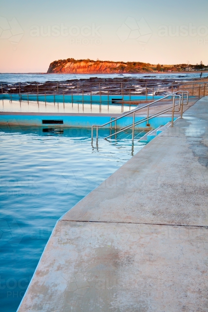 Evening light over tidal bathing pools with a bluff brightly illuminated in the distance - Australian Stock Image