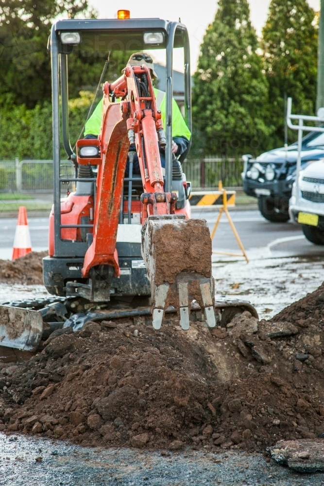 Excavator digging a hole in the road to fix broken water main - Australian Stock Image