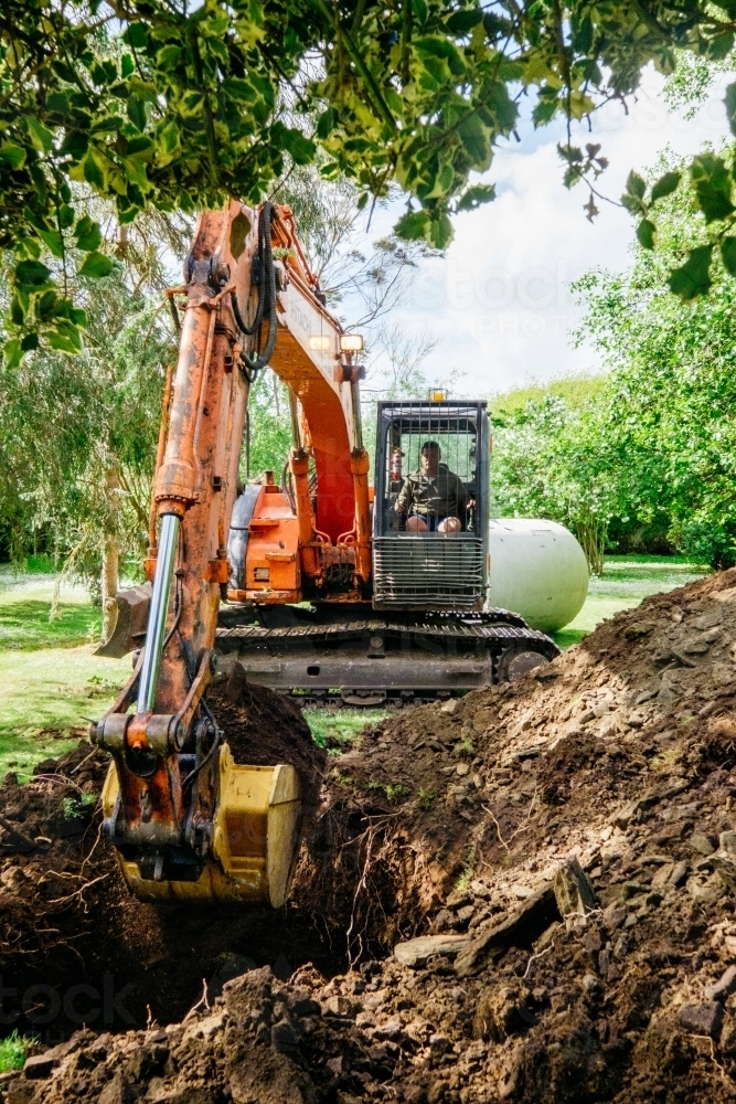 Image of Excavator digging hole in rural garden Austockphoto