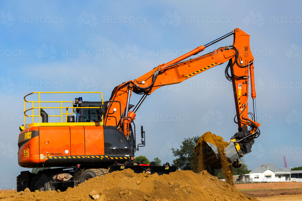 Excavator earthmoving equipment working on dirt pile at construction site - Australian Stock Image