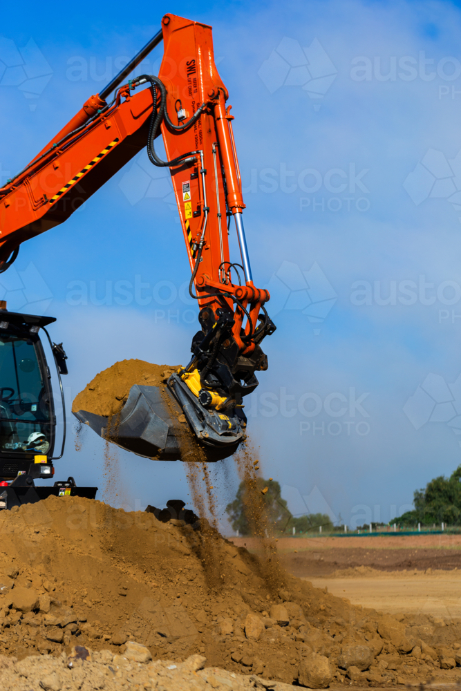 Excavator earthmoving equipment working on dirt pile at construction site - Australian Stock Image