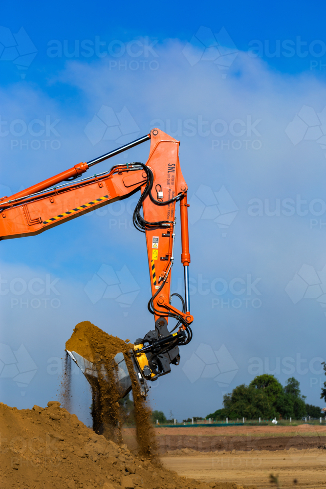 Excavator earthmoving equipment working on dirt pile at construction site - Australian Stock Image