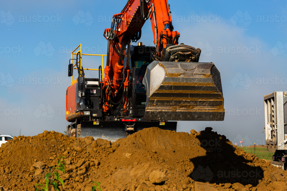 Excavator earthmoving equipment working on dirt pile at construction site - Australian Stock Image