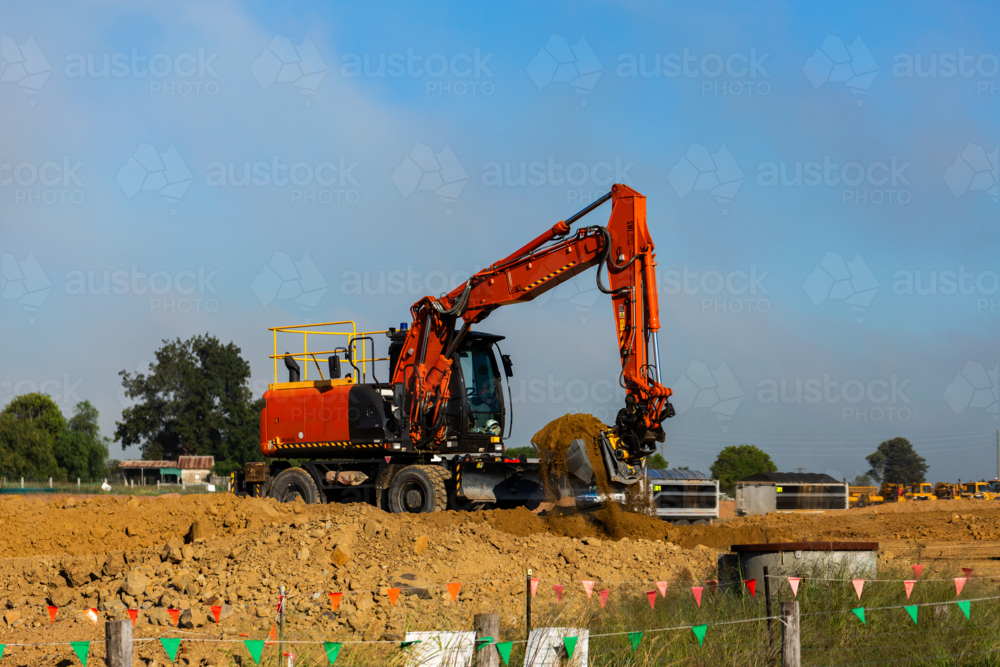 Excavator earthmoving equipment working on dirt pile at construction site - Australian Stock Image