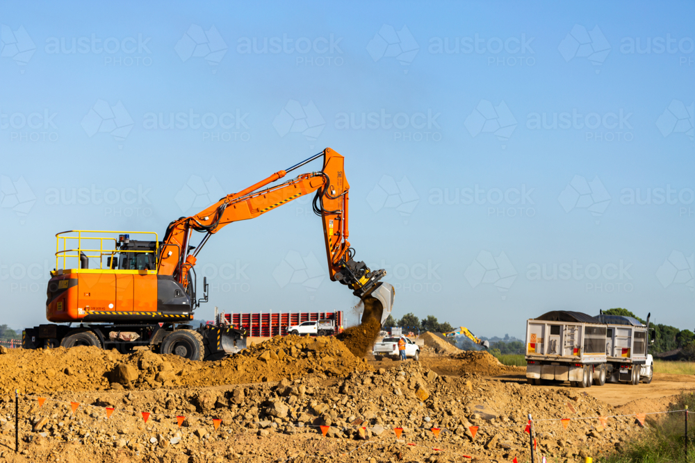 Excavator earthmoving equipment working on dirt pile at construction site beside truck - Australian Stock Image