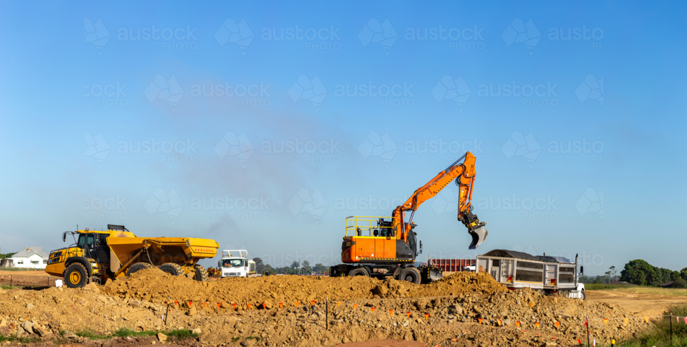 Excavator earthmoving equipment working on dirt pile at construction site beside truck - Australian Stock Image