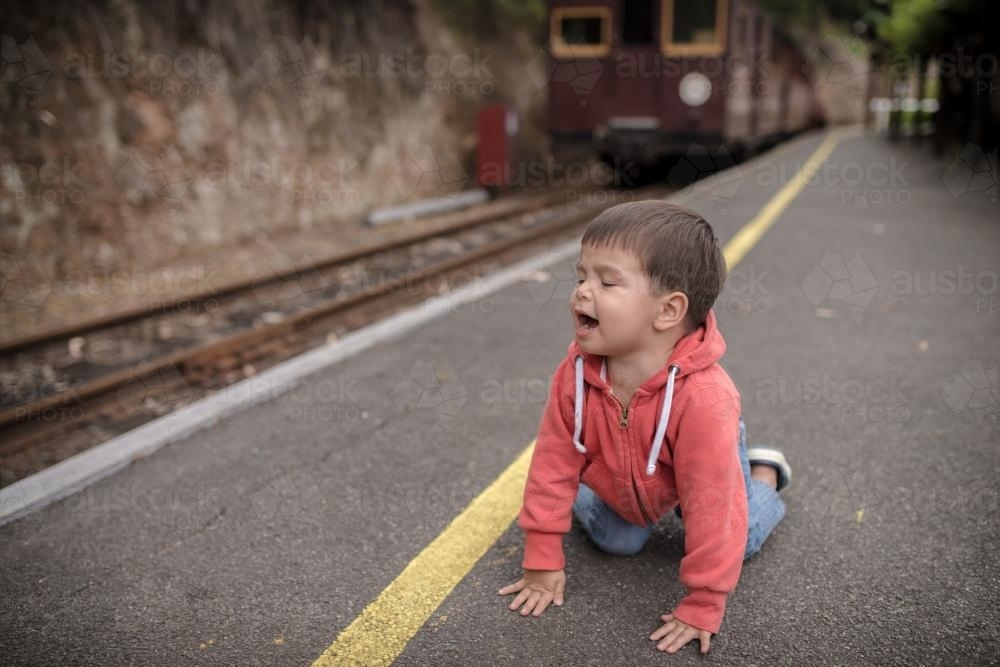 Excited 2 year old mixed race boy on hands and knees an a train platform - Australian Stock Image