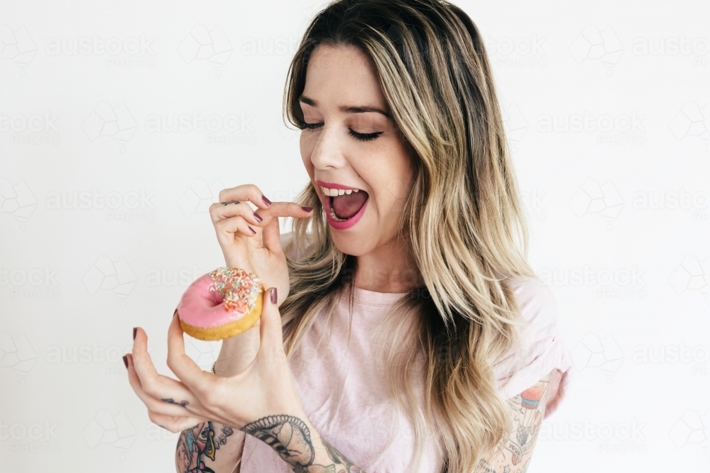 Excited girl about to bite into a pink iced donut - Australian Stock Image