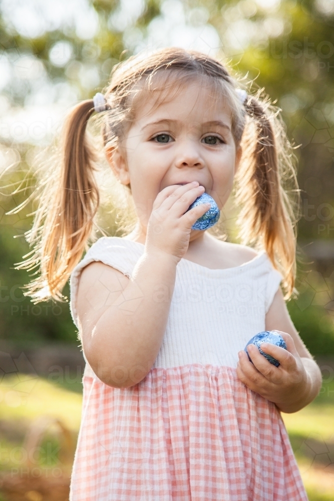 Excited little girl finds blue Easter eggs during Easter egg hunt - Australian Stock Image