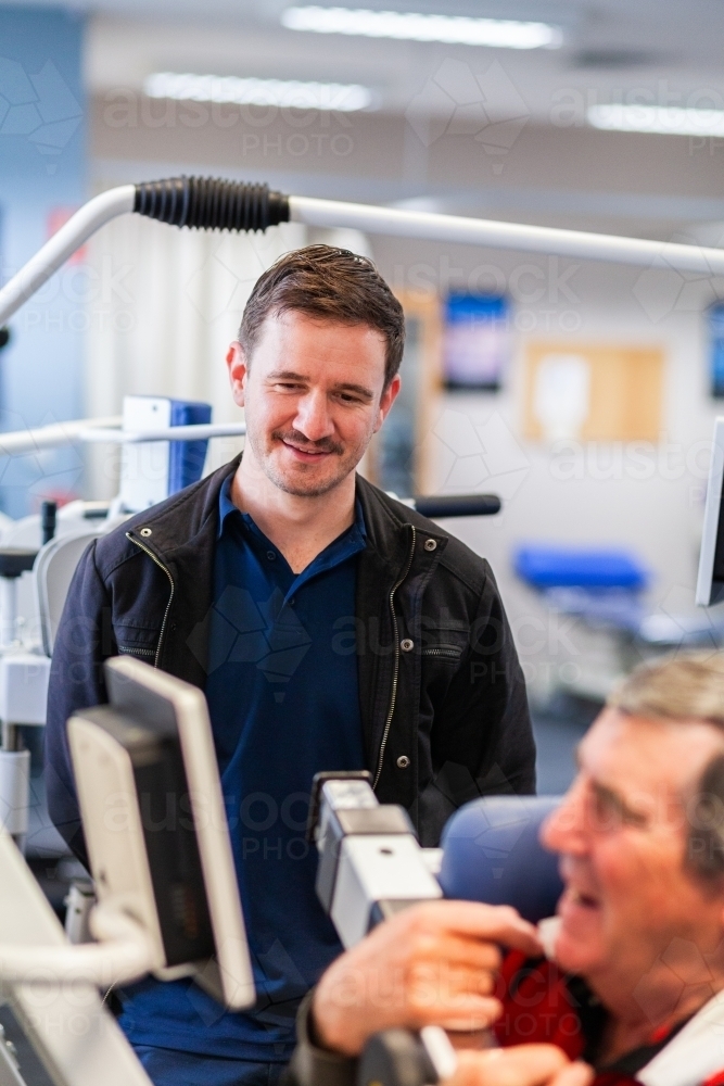 exercise therapy equipment at physiotherapy clinic with man using it and smiling physio - Australian Stock Image